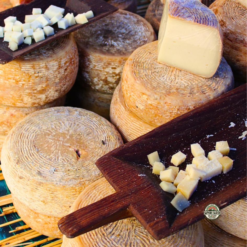 Ein Laib Pecorino aus Sardinien, aus welchem mit einem sardischen Hirtenmesser ein großes Stück herausgeschnitten wurde. Der Käse liegt auf einem Holzbrett und es ist eine abendliche Stimmung.