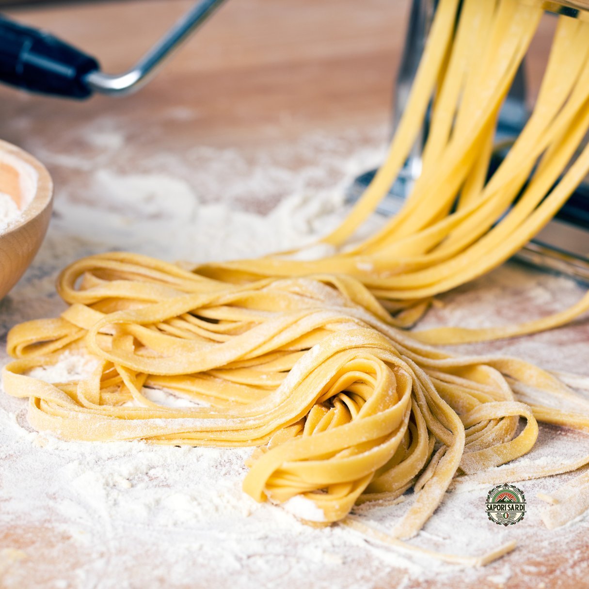 Frische Pasta welche gerade durch eine Pasta Maschine gedreht wurde. sie liegt auf einem Holztisch mit Mehl.