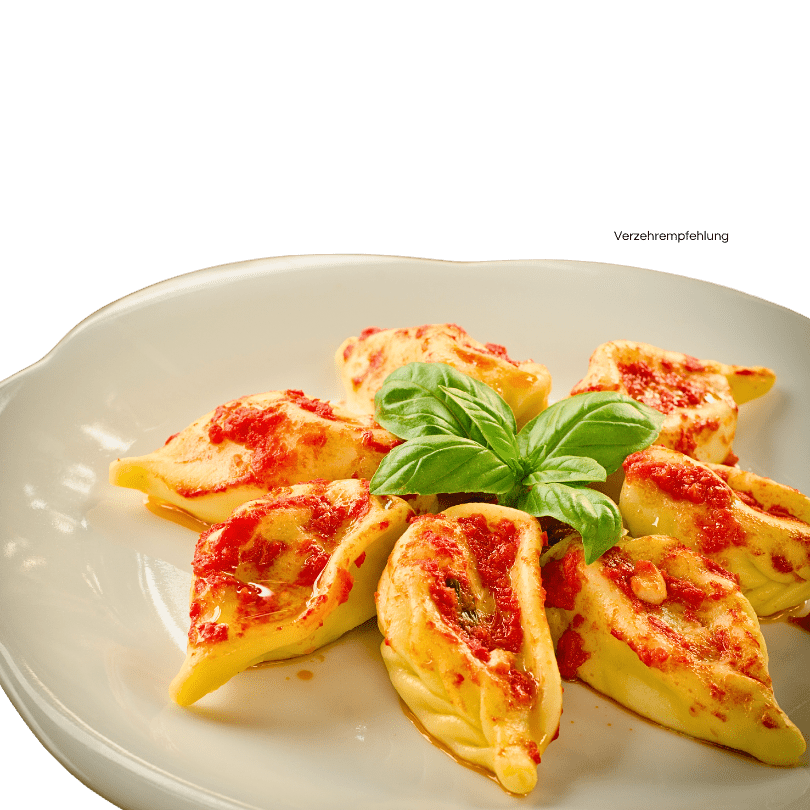 Culurgiones mit einer Tomatensauce auf einem Teller angerichtet. Verziert mit Basilikum.