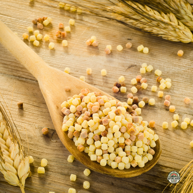 Fregola Sarda aus Hartweizengries auf einem Holztisch mit Weizen.