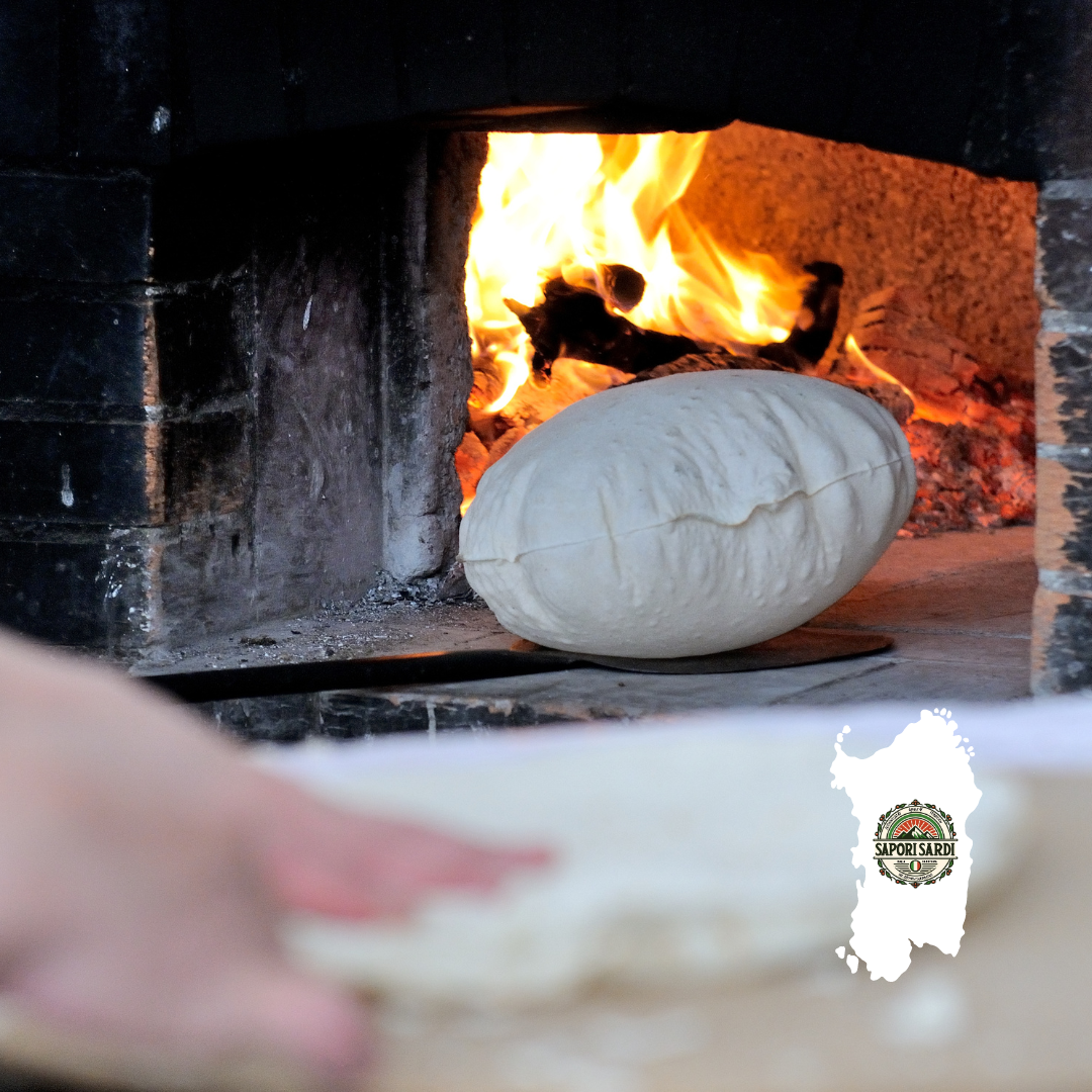 Pane Carasau im vor einem ofen liegend. Es wird gerade aus einem Holzofen herausgeholt und der Teig ist sichtbar aufgeblasen. Unten rechts sieht man das Logo von Sapori Sardi auf einer weißen Sardinien Karte.