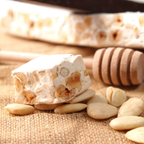 Stück sardischer Torrone mit ganzen Mandeln auf rustikalem Untergrund, daneben Honiglöffel und Mandeln