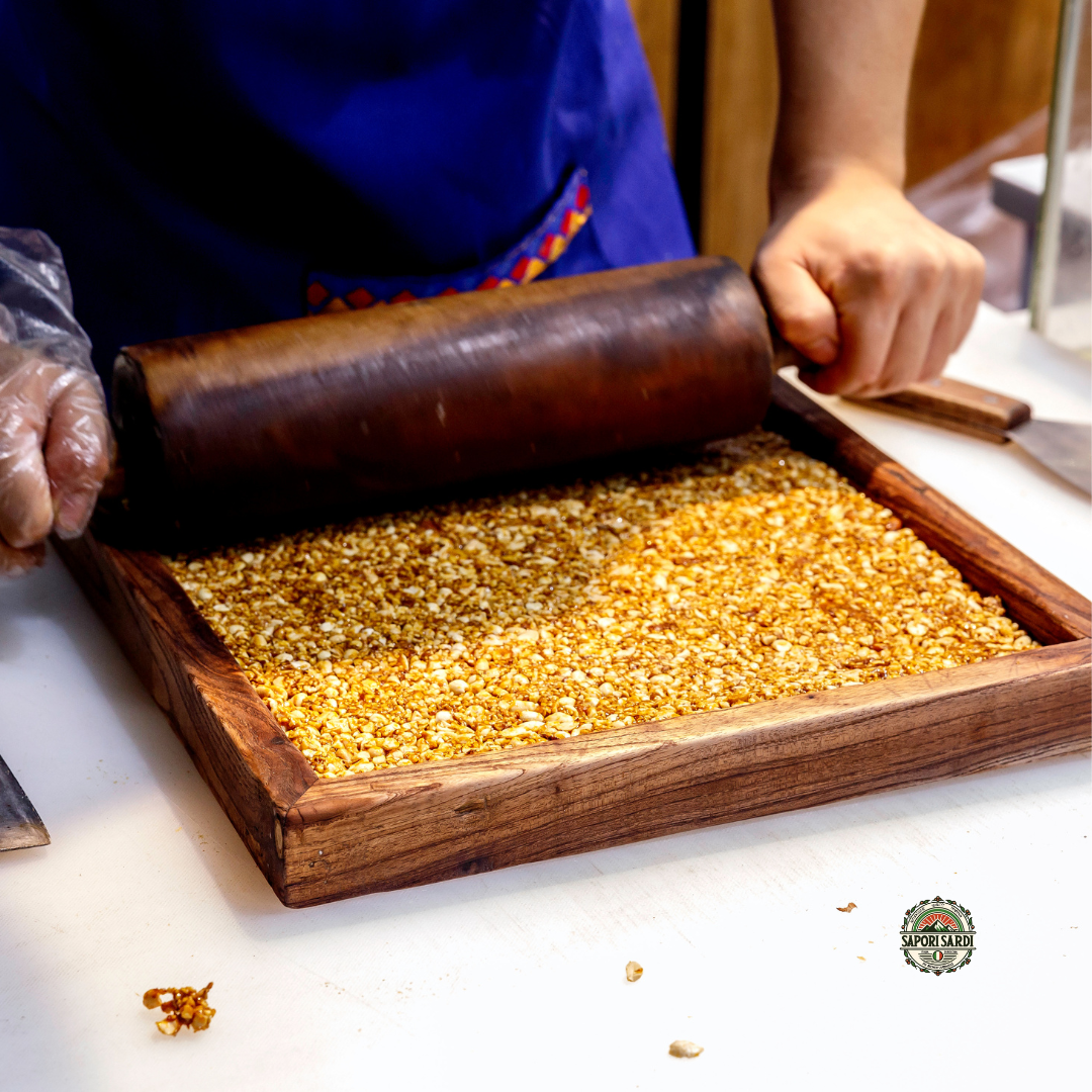 Torrone wird in einem Holzrahmen per Hand mit einem Nudelholz ausgerollt. Gezeigt wird die Traditionelle Art Torrone zu formen.Unten rechts ist das Logo von Sapori Sardi zu sehen.